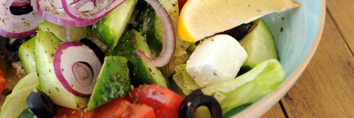 A vibrant bowl of Greek salad with fresh vegetables, feta cheese, and a lemon slice.
